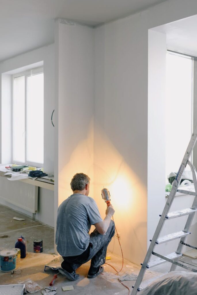 Back view of anonymous male in dirty clothes renovating walls in home while holding lamp